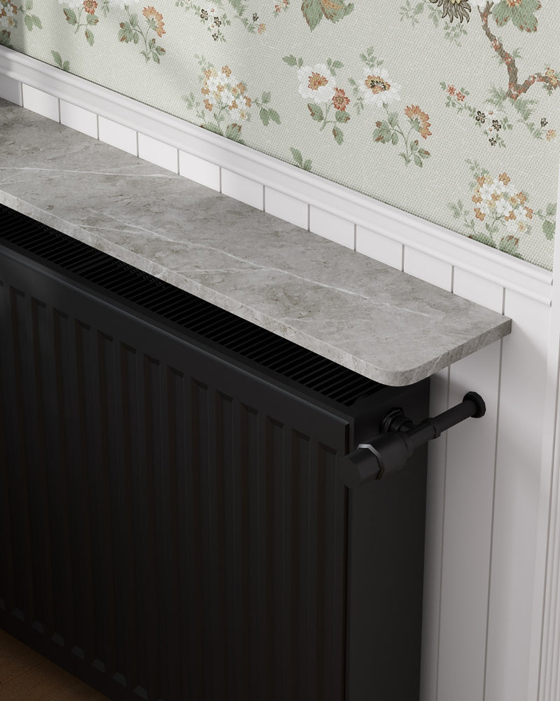 Close detail of a grey marble Loby radiator shelf fitted above a black radiator against floral wallpaper and white panelling