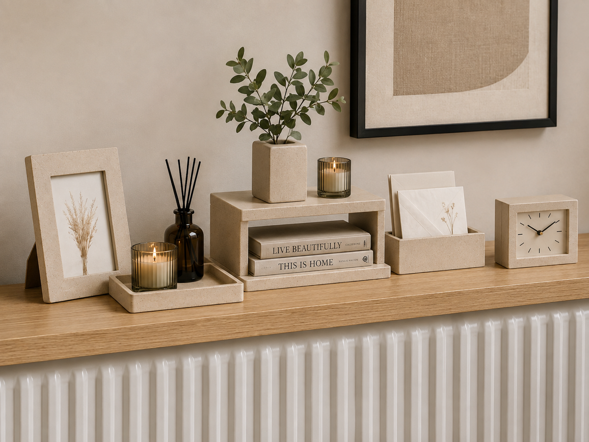 An oak radiator shelf styled with a photo frame, candles, a reed diffuser, a potted eucalyptus, books, a letter holder and a small clock