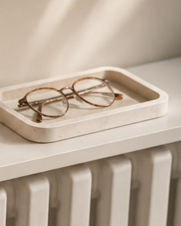 A pair of glasses resting in a shallow cream decorative tray on a white radiator shelf
