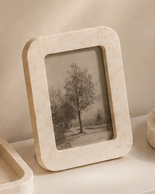 A cream stone-effect photo frame holding a pencil sketch of a tree, standing on a shelf