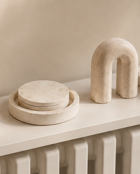 A cream arch sculpture beside a set of round coasters in a matching dish on a white radiator shelf