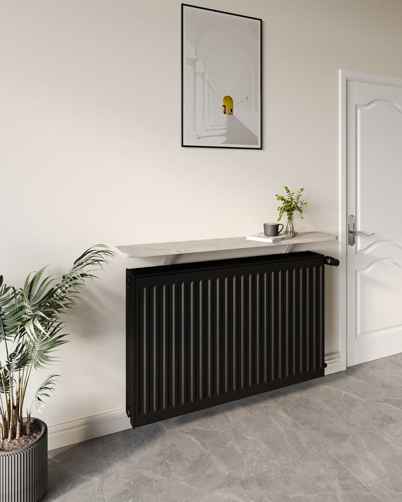 A white marble Loby radiator shelf above a black radiator in a styled hallway, with a framed print above and a plant beside it